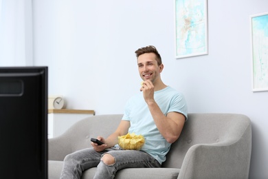 Man eating potato chips while watching TV in living room