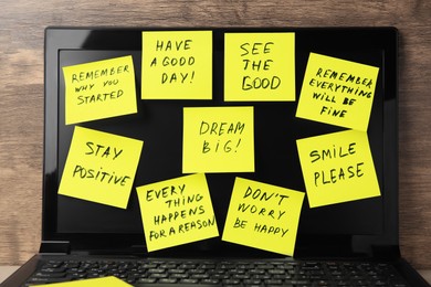 Photo of Paper notes of life-affirming phrases on laptop against wooden background