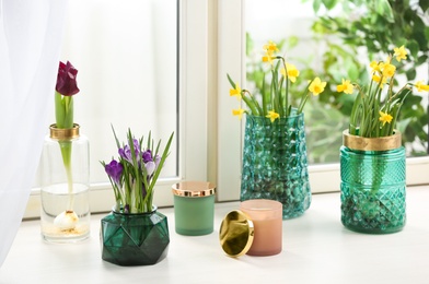 Photo of Different beautiful spring flowers and candles on window sill