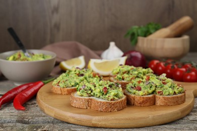 Photo of Slices of bread with tasty guacamole and ingredients on wooden table, closeup