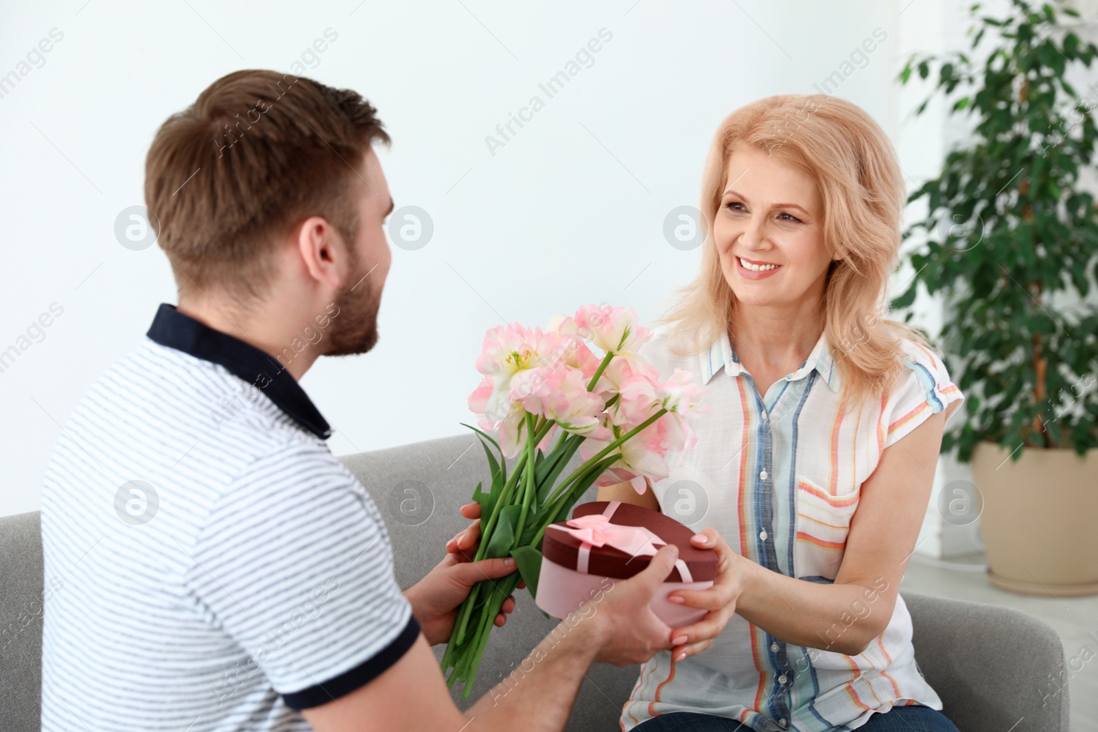 Photo of Young man congratulating his mature mom at home. Happy Mother's Day