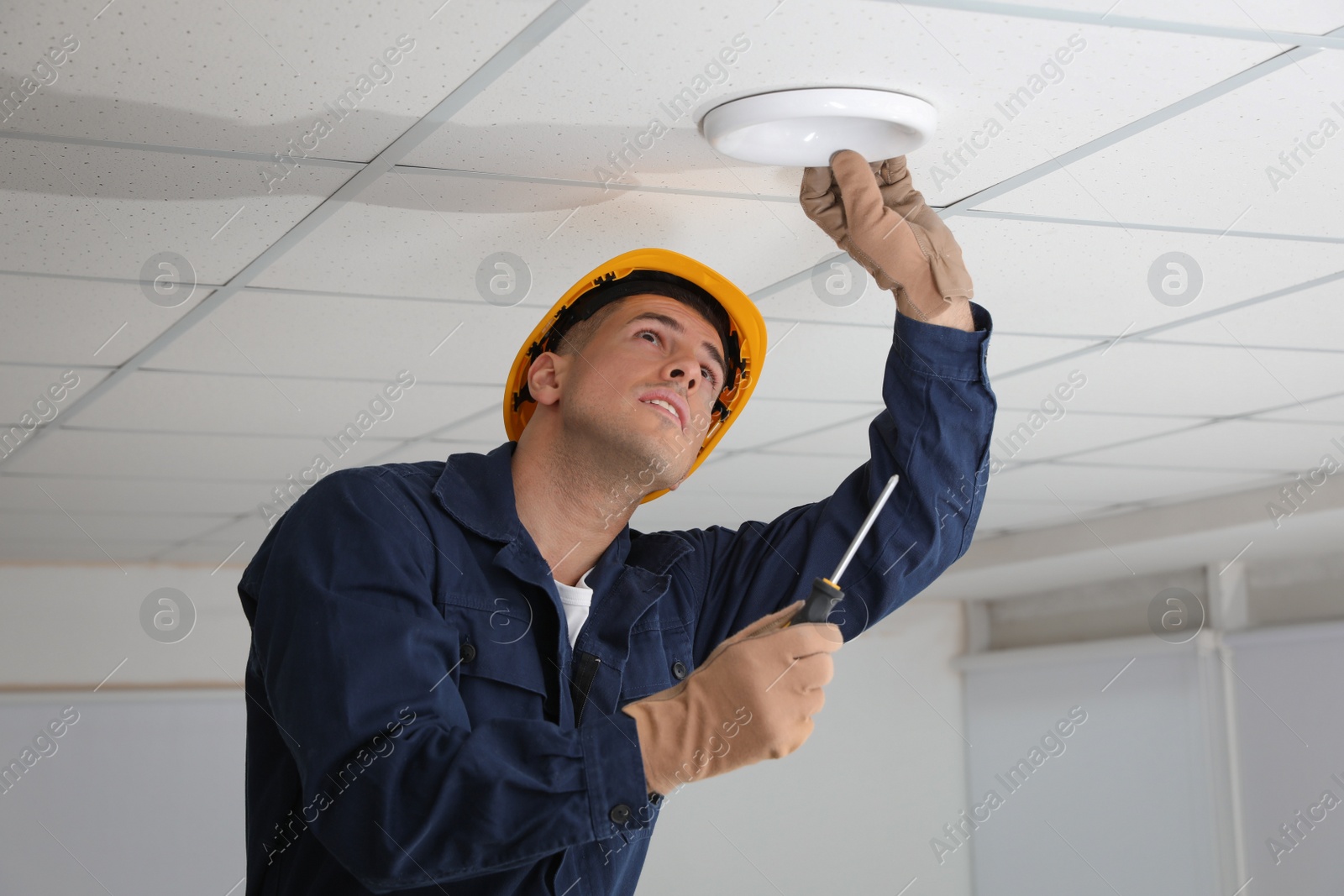 Photo of Electrician with screwdriver repairing ceiling lamp indoors
