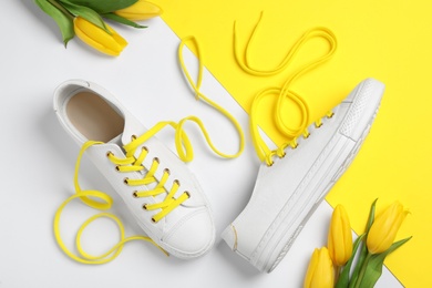 Photo of Stylish sneakers with yellow shoe laces and tulips on color background, flat lay