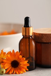 Photo of Bottle and jar of cosmetic products with beautiful calendula flowers on light grey table, closeup