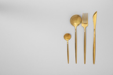 Photo of Stylish golden cutlery set on gray background, flat lay. Space for text