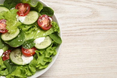Delicious salad in bowl on white wooden table, top view. Space for text