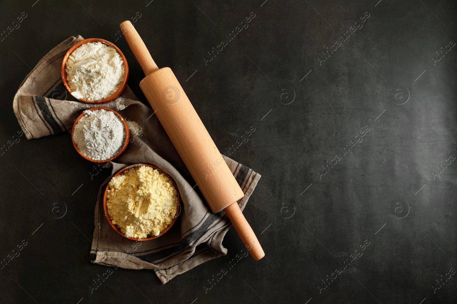 Photo of Rolling pin and different types of flour on black table, top view. Space for text