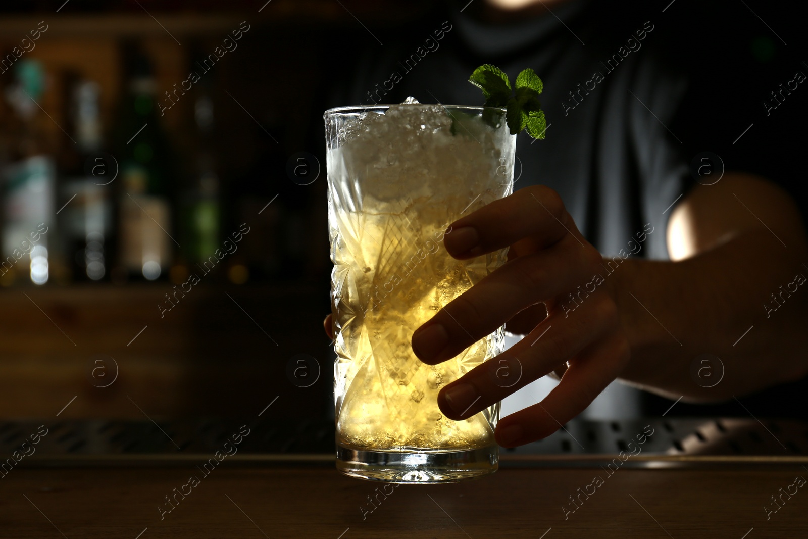 Photo of Bartender holding glass of fresh alcoholic cocktail at bar counter, closeup