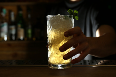 Bartender holding glass of fresh alcoholic cocktail at bar counter, closeup