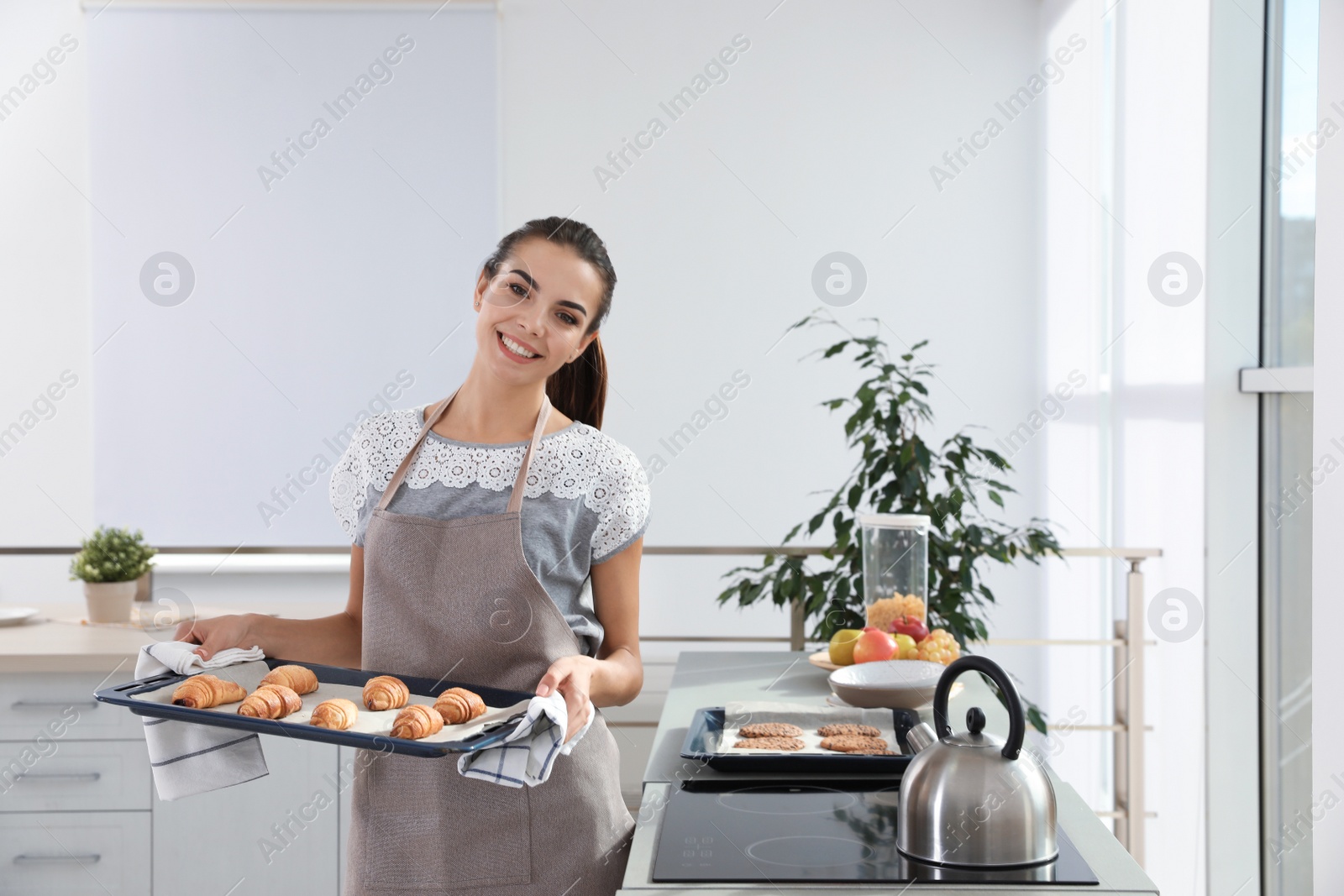 Photo of Young woman holding oven sheet with homemade croissants in kitchen