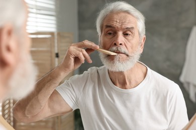 Photo of Senior man combing mustache near mirror in bathroom