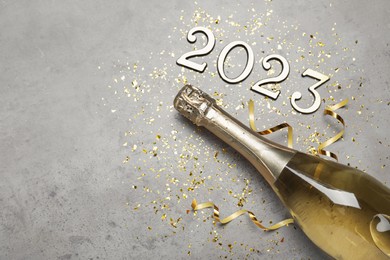 Bottle of sparkling wine, festive decor and number 2023 on grey background, flat lay with space for text. Happy New Year