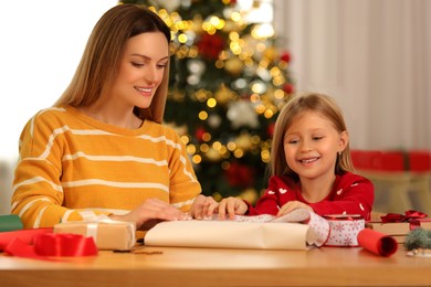Christmas celebration. Mother and her little daughter wrapping gift at home