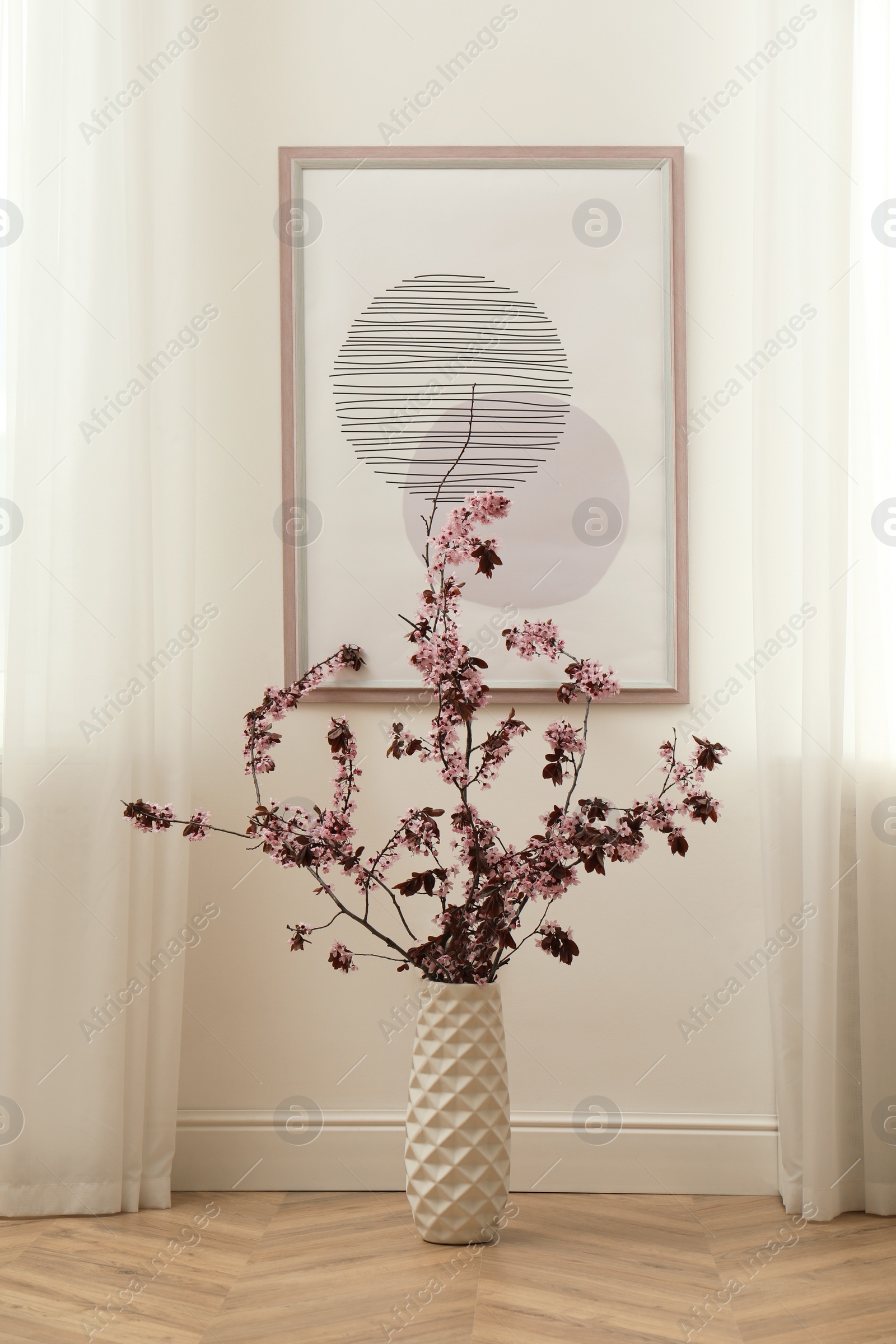 Photo of Blossoming tree twigs in vase on floor near wall with picture indoors