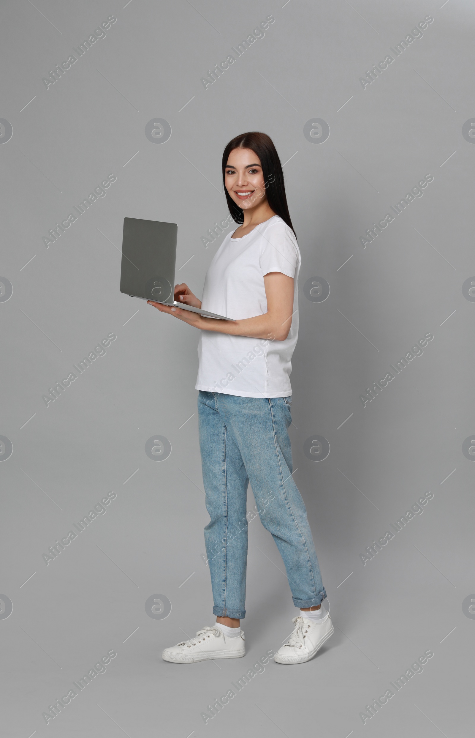 Photo of Young woman with modern laptop on light grey background