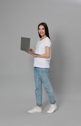 Young woman with modern laptop on light grey background