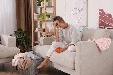 Photo of Tired young mother sitting on sofa in messy living room