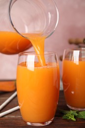 Photo of Pouring freshly made carrot juice into glass on wooden table