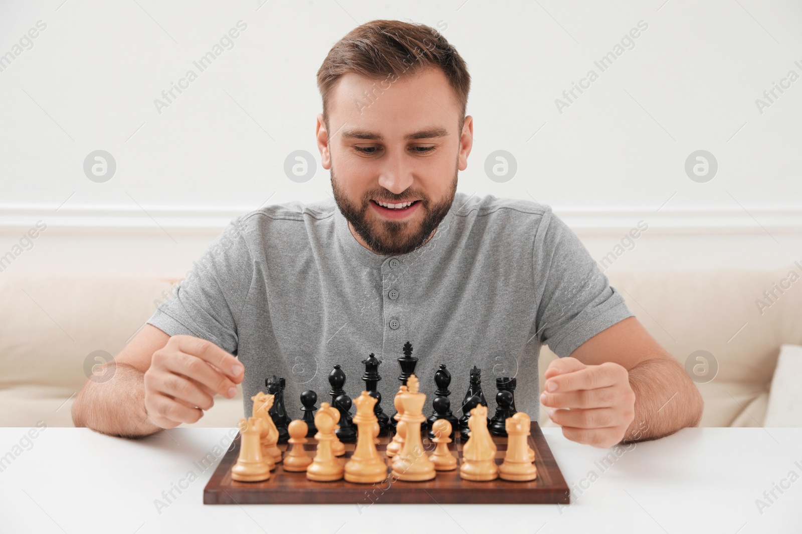 Photo of Happy young man playing chess at white table indoors