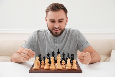 Happy young man playing chess at white table indoors