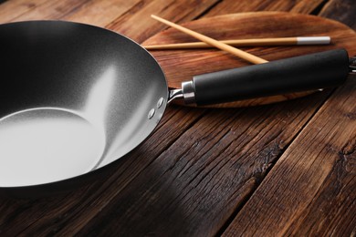 Photo of Empty iron wok and chopsticks on wooden table, closeup