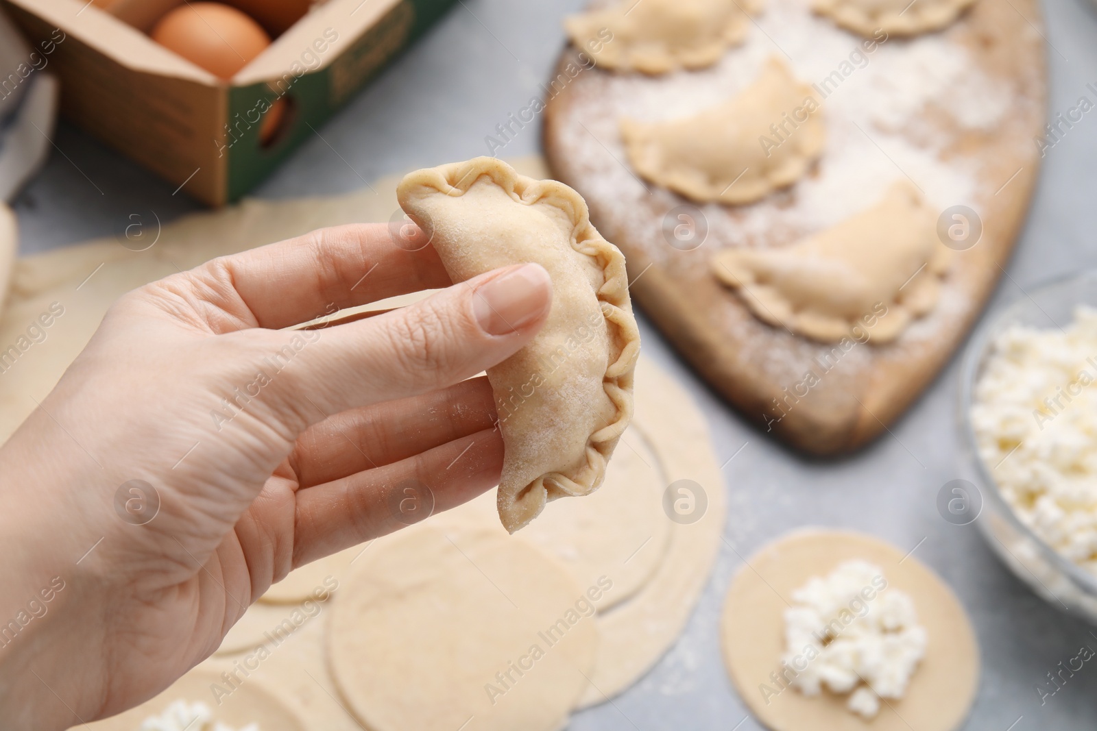 Photo of Woman holding dumplings (varenyky) with cottage cheese at grey table, closeup