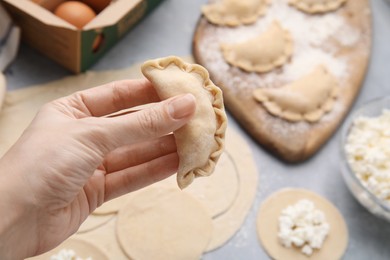 Photo of Woman holding dumplings (varenyky) with cottage cheese at grey table, closeup