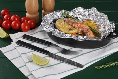 Photo of Tasty salmon baked in foil with citrus fruits and rosemary served on green wooden table