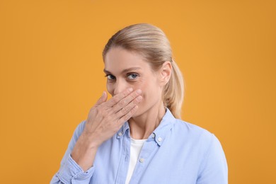 Portrait of embarrassed woman covering mouth with hand on orange background