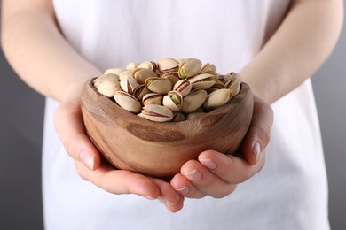 Photo of Woman holding tasty pistachios in bowl on grey background, closeup