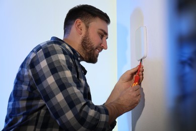Man installing security alarm system on light wall at home