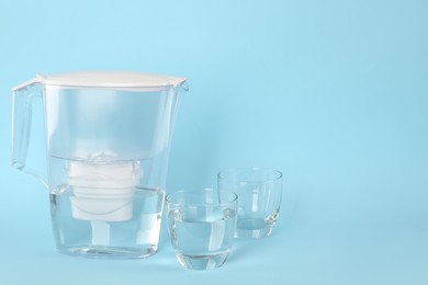 Photo of Filter jug and glasses with purified water on light blue background. Space for text