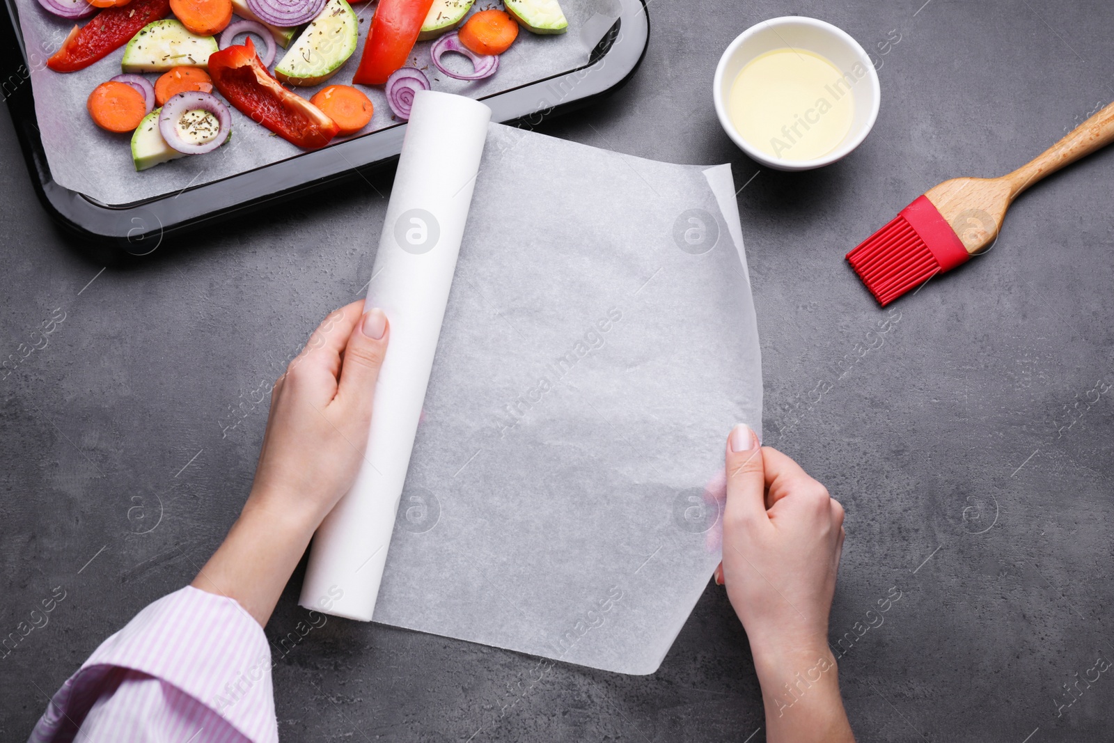 Photo of Woman holding parchment paper over dark grey table, top view. Baking vegetables