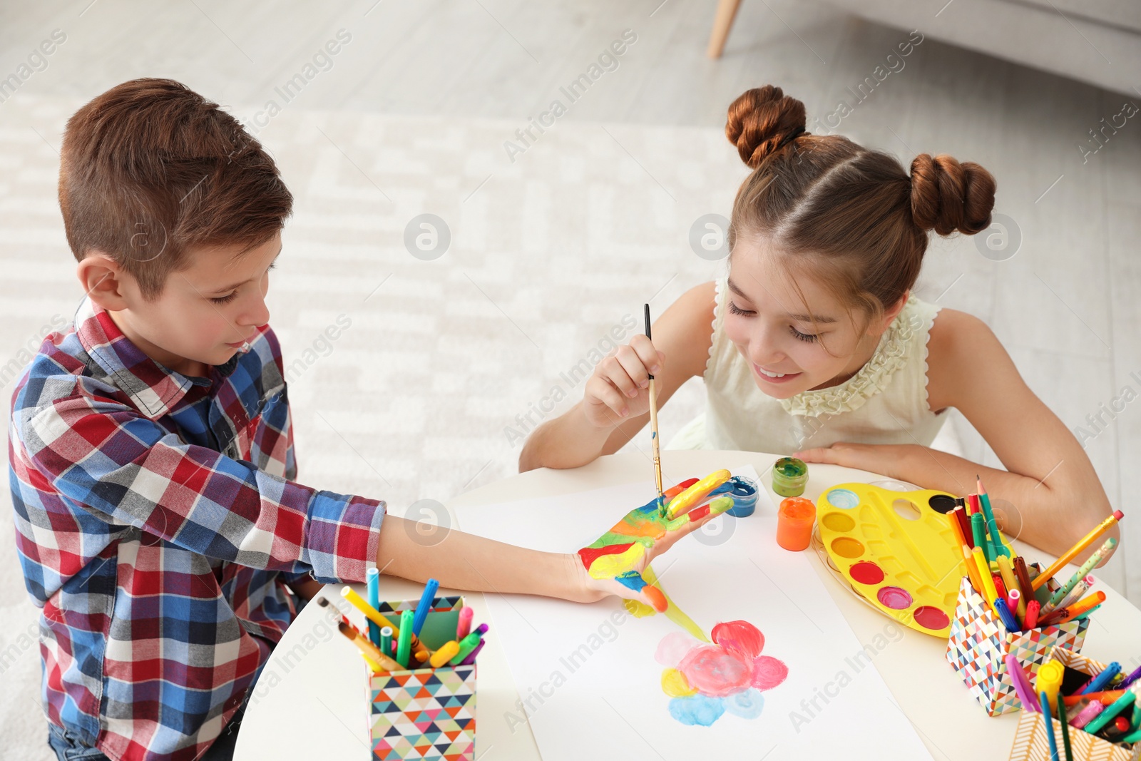 Photo of Little children painting hands at table indoors