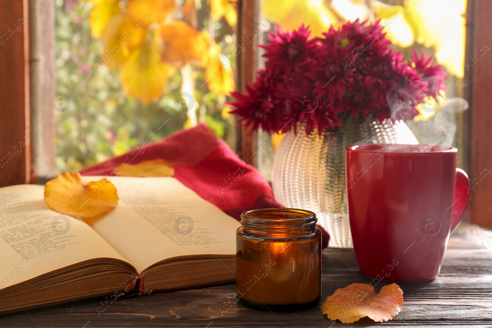 Photo of Beautiful chrysanthemum flowers, cup of hot drink and book on wooden table indoors. Autumn still life