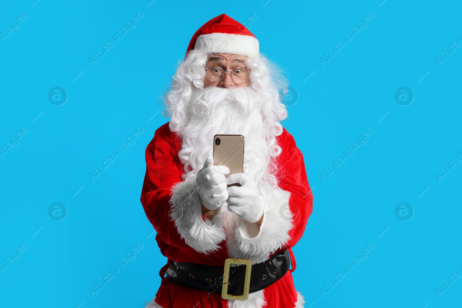 Photo of Merry Christmas. Santa Claus using smartphone on light blue background