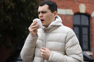Sick young man with tissue on city street. Cold symptoms