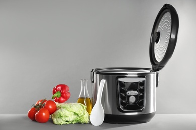 Photo of Modern multi cooker and products on table against grey background. Space for text