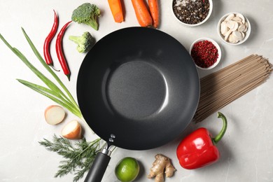 Empty iron wok surrounded by raw ingredients on light table, flat lay