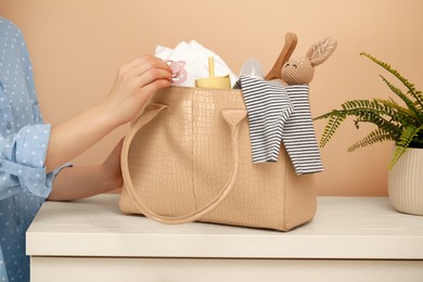 Photo of Woman putting baby`s pacifier into mother`s bag on white chest of drawers indoors, closeup