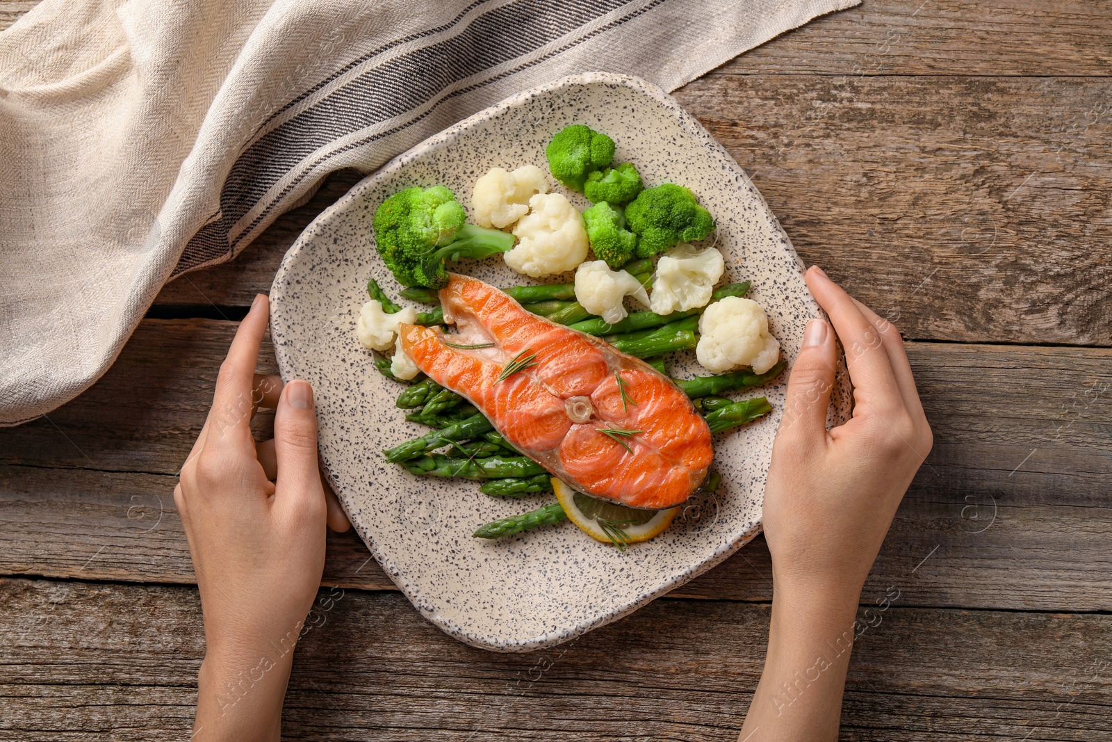 Photo of Healthy meal. Woman with plate of tasty grilled salmon and vegetables at wooden table, top view