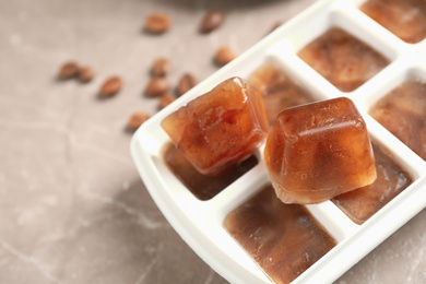 Photo of Ice cube tray with frozen coffee on grey table, closeup. Space for text