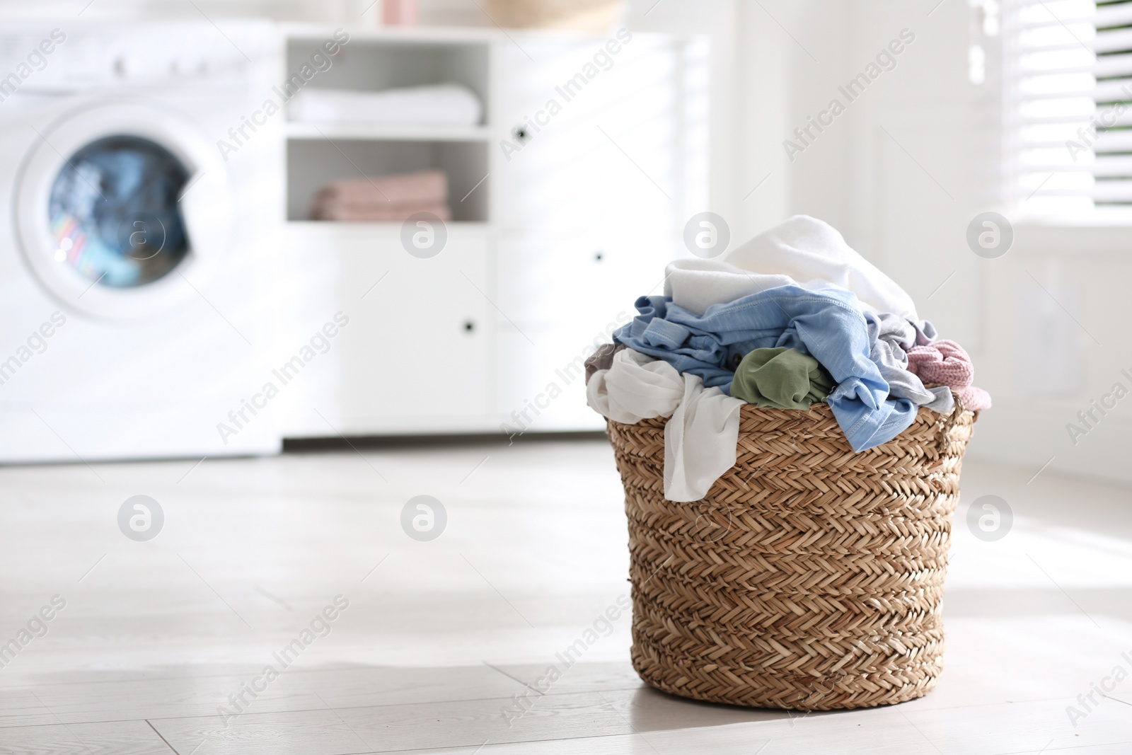 Photo of Wicker basket with dirty laundry on floor indoors, space for text