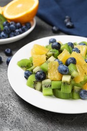 Photo of Plate of tasty fruit salad on grey textured table, closeup