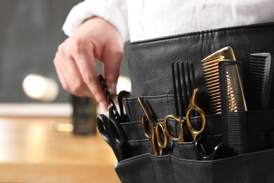 Photo of Hairstylist with professional tools in waist pouch in salon, closeup