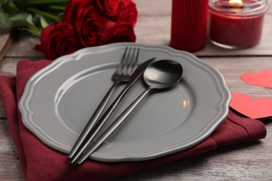 Photo of Romantic place setting with red roses, candle and decorative hearts on wooden table. St. Valentine's day dinner