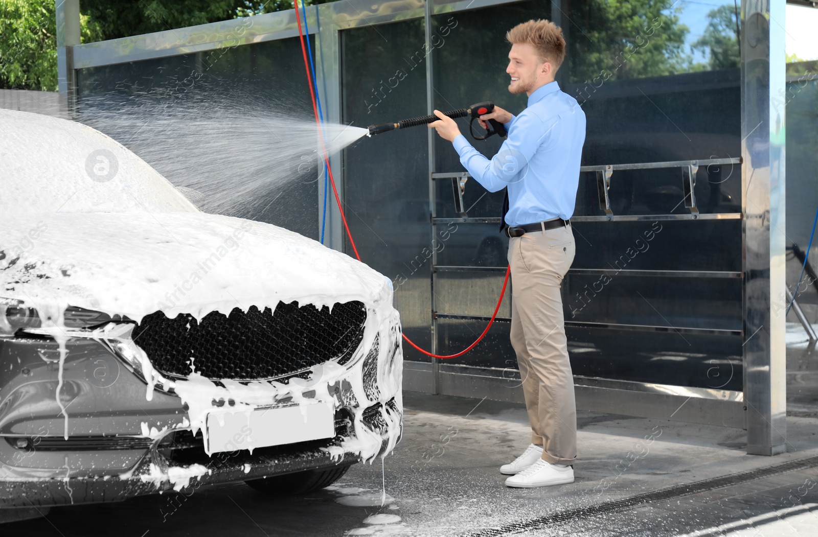 Photo of Businessman cleaning auto with high pressure water jet at self-service car wash