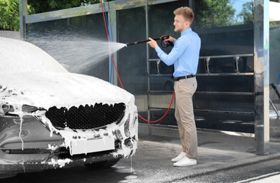 Businessman cleaning auto with high pressure water jet at self-service car wash