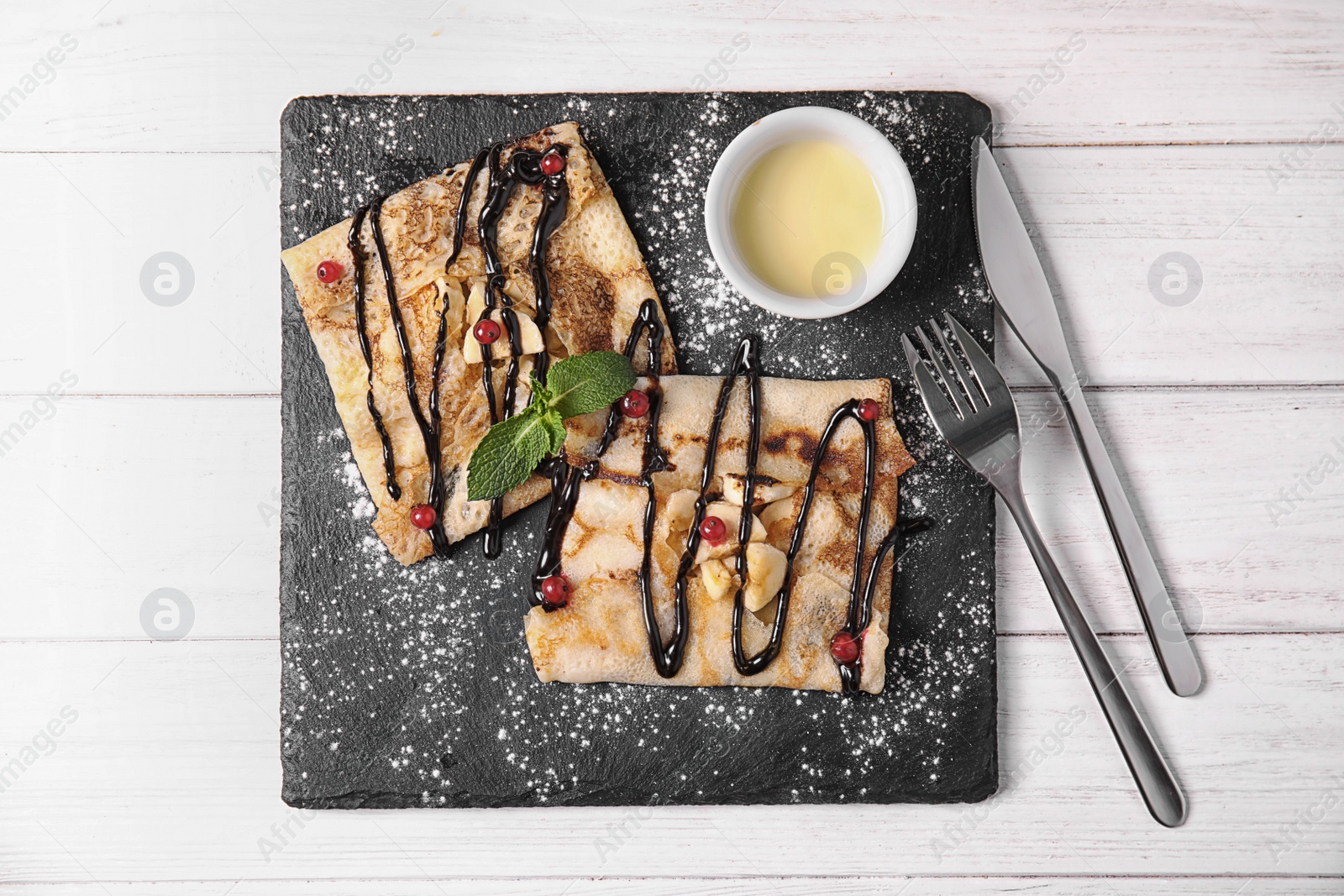 Photo of Thin pancakes served with sauce and berries on slate plate, top view