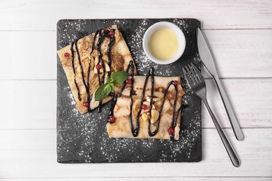 Photo of Thin pancakes served with sauce and berries on slate plate, top view